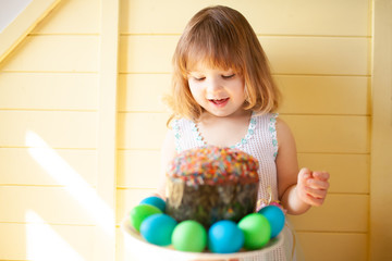 Cute girl with Easter eggs and Easter cake with yellow wooden background