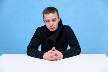 Concept studio portrait of a young man on a blue background sitting on a cube.