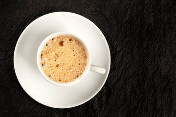 A cup of regular coffee with foam on a dark black background with a place for text