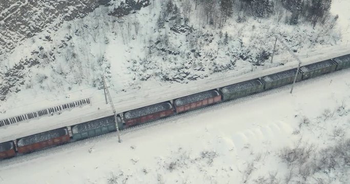 Freight train with coal on Trans Siberian winding two-sided railways near river at winter frozen day in Ural Mountains in Russia - Aerial drone view
