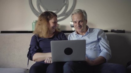 Excited couple with laptop celebrating success. Middle aged man and woman sitting on couch, using computer, getting great news and giving high five. Win or victory concept - Powered by Adobe