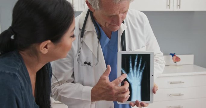 Doctor using tablet computer with x-ray of hand explaining injury to patient