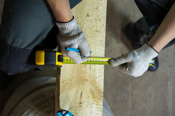 A worker at a construction site where repairs are underway, measures with a pencil how much to cut off the wooden board