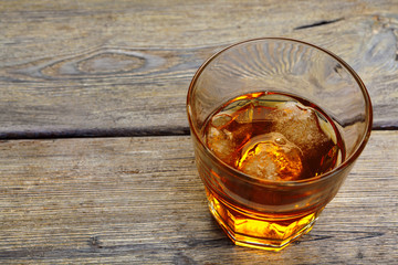 Glass of whiskey on ice with bottle on wood bar