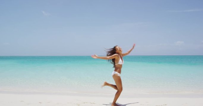 Happy joyful carefree girl jumping of joy on fun beach vacation getaway in tropical travel holiday destination. Happiness excitement, freedom, success in weight loss concept. Asian bikini body woman.