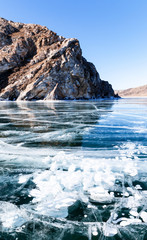 Lake Baikal in February sunny day. Beautiful unusual landscape with white bubbles of bottom gases in transparent clear ice near coastal rocks. Winter travel on the ice of a frozen lake