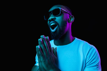 The retro wave or synth wave portrait of a young happy smiling african man in sunglasses at studio. High Fashion male model in colorful bright neon lights posing on black background. Art design