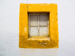 Obraz na płótnie Canvas Old window in a typical yellow frame on a white wall, Evora, Portugal.