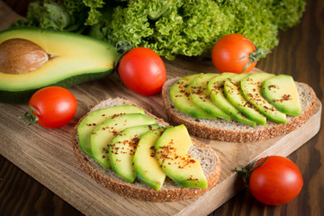 macro photo of sliced avocado with tomatoes on a cutting board on wooden background. Healthy organic food concept.