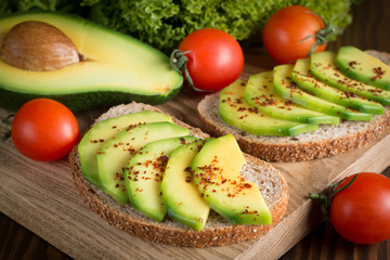 macro photo of sliced avocado with tomatoes on a cutting board on wooden background. Healthy organic food concept.