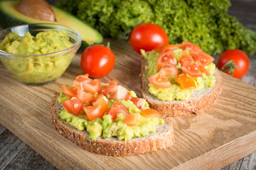 macro photo of sliced avocado with tomatoes on a cutting board on wooden background. Healthy organic food concept.