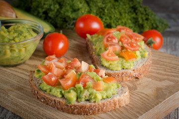 macro photo of sliced avocado with tomatoes on a cutting board on wooden background. Healthy organic food concept.