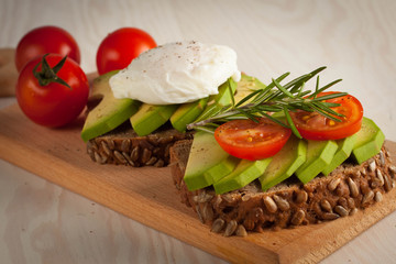 Avocado toast, cherry tomato and poached eggs on wooden background. Breakfast with vegetarian food, healthy diet concept.