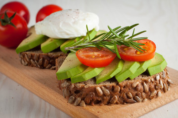 Avocado toast, cherry tomato and poached eggs on wooden background. Breakfast with vegetarian food, healthy diet concept.