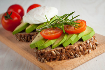 Avocado toast, cherry tomato and poached eggs on wooden background. Breakfast with vegetarian food, healthy diet concept.