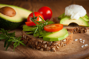 Avocado toast, cherry tomato and poached eggs on wooden background. Breakfast with vegetarian food, healthy diet concept.