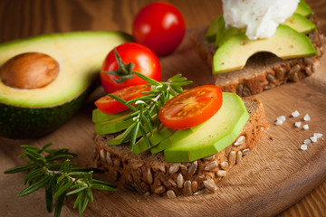 Avocado toast, cherry tomato and poached eggs on wooden background. Breakfast with vegetarian food, healthy diet concept.
