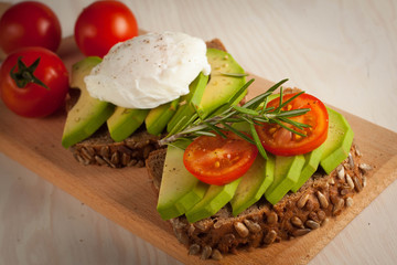 Avocado toast, cherry tomato and poached eggs on wooden background. Breakfast with vegetarian food, healthy diet concept.
