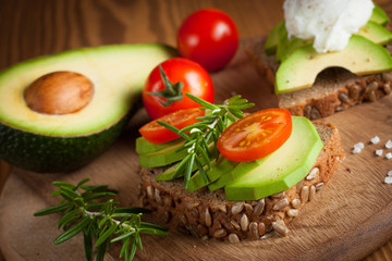 Avocado toast, cherry tomato and poached eggs on wooden background. Breakfast with vegetarian food, healthy diet concept.