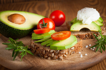 Avocado toast, cherry tomato and poached eggs on wooden background. Breakfast with vegetarian food, healthy diet concept.