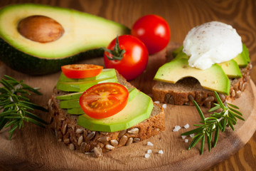 Avocado toast, cherry tomato and poached eggs on wooden background. Breakfast with vegetarian food, healthy diet concept.