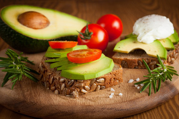 Avocado toast, cherry tomato and poached eggs on wooden background. Breakfast with vegetarian food, healthy diet concept.