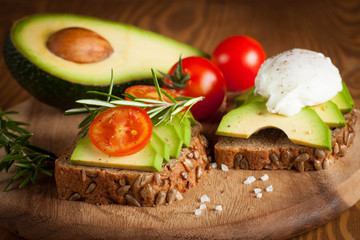 Avocado toast, cherry tomato and poached eggs on wooden background. Breakfast with vegetarian food, healthy diet concept.