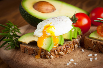Avocado toast, cherry tomato and poached eggs on wooden background. Breakfast with vegetarian food, healthy diet concept.