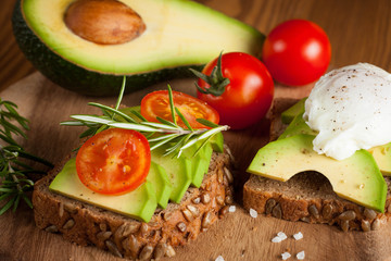 Avocado toast, cherry tomato and poached eggs on wooden background. Breakfast with vegetarian food, healthy diet concept.