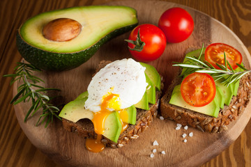 Avocado toast, cherry tomato and poached eggs on wooden background. Breakfast with vegetarian food, healthy diet concept.
