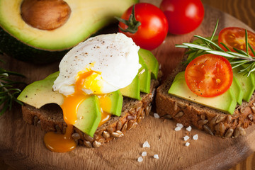 Avocado toast, cherry tomato and poached eggs on wooden background. Breakfast with vegetarian food, healthy diet concept.