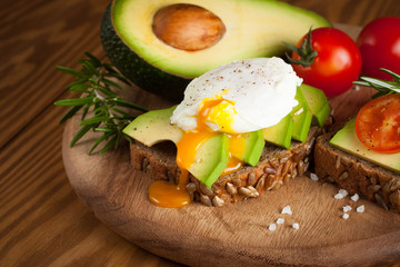 Avocado toast, cherry tomato and poached eggs on wooden background. Breakfast with vegetarian food, healthy diet concept.
