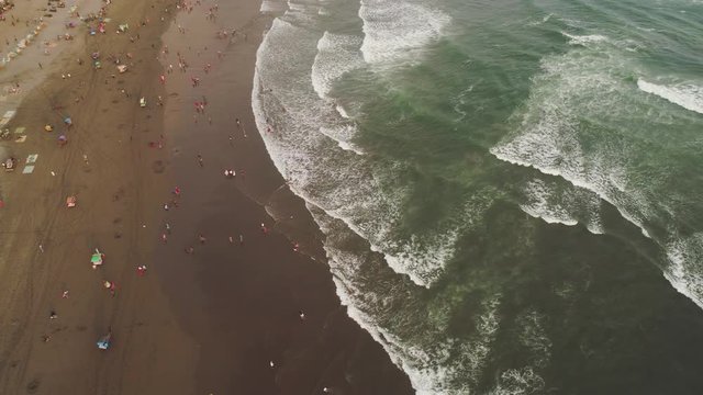sandy beach parangtritis near ocean with big waves, people in tropical resort at sunset. Yogyakarta, Indonesia. aerial view seascape, ocean and beautiful beach. Travel concept. Indonesia, java