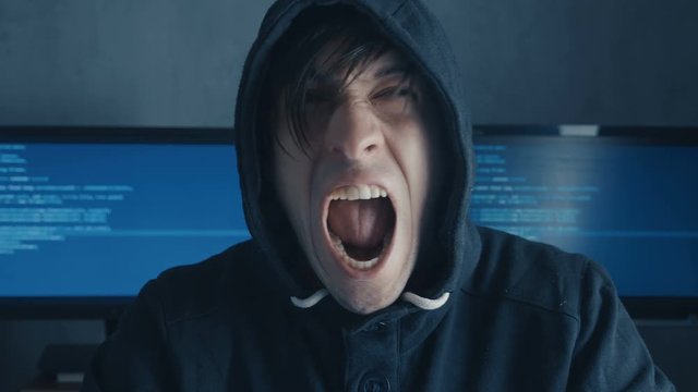 Portrait of Angry Hacker Programmer screams and shows aggression while working at the computer. Stress in the workplace.