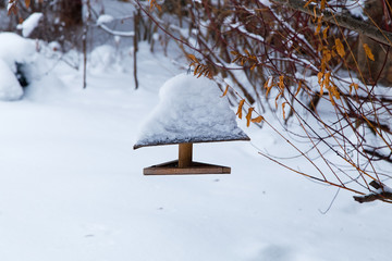 Wooden Bird feeder in the winter snow garden. Homemade house for birds with snow on roof.
