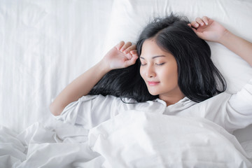 Beautiful young pretty Asian woman wake up and make happy smile with white shirt at the white bed in the morning.  