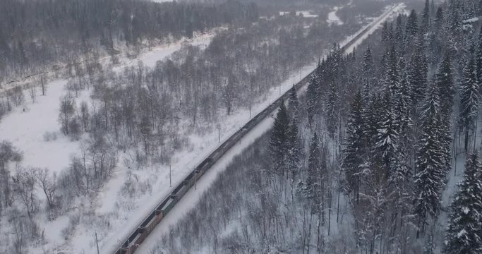 Freight train with coal on Trans Siberian winding two-sided railways near river at winter frozen day in Ural Mountains in Russia - Aerial top view