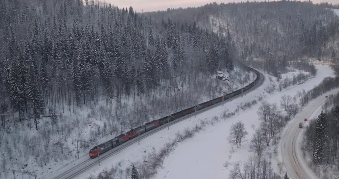 Freight train with coal on Trans Siberian winding two-sided railways near river at winter frozen day in Ural Mountains in Russia - Aerial top view
