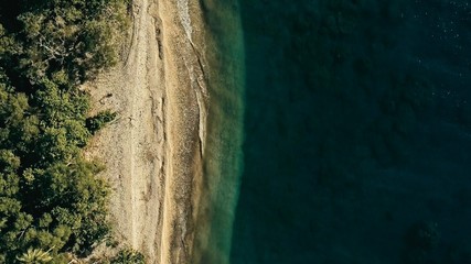 stunning aerial drone minimal geometric image of a remote tropical sea ocean shore with sandy beach lush rainforest jungle and crystal clear azure blue water from top looking down at sunset