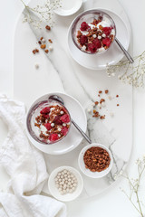 Flat lay with two glasses of layered granola and yogurt with raspberries on a marble tray 