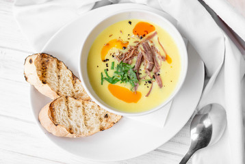 Corn soup puree with toast in white bowl on white wooden background, top view