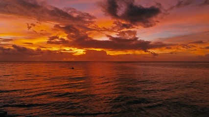 Naklejka na ściany i meble stunning beautiful aerial drone image of a red tropical sunset above the sea ocean with two man in a canoe fishing