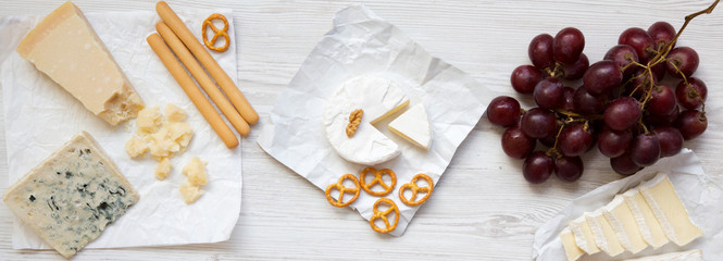 Tasting cheese with grapes, bread sticks, walnuts and pretzels on wooden surface, overhead view. Food for wine. Flat lay. From above.