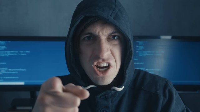 Portrait of Angry Hacker Programmer screams and shows aggression while working at the computer. Stress in the workplace.