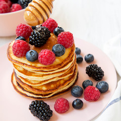 Tasty pancakes with berries and honey on a pink plate, side view. Close-up.