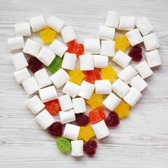 Heart made of candies over white wooden surface, overhead view. From above, flat lay, top view.
