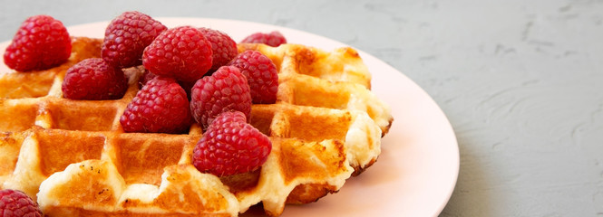 Belgian waffle with raspberries on pink plate over concrete background, side view. Closeup.