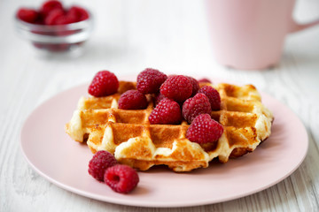 Belgian waffle with raspberries on pink plate over white wooden background, side view. Closeup.