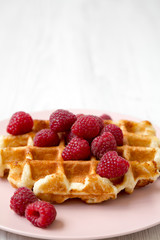 Belgian waffle with raspberries on pink plate over white wooden background, side view. Copy space.