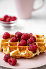 Belgian waffle with raspberries on pink plate over white wooden surface, side view. Close-up.
